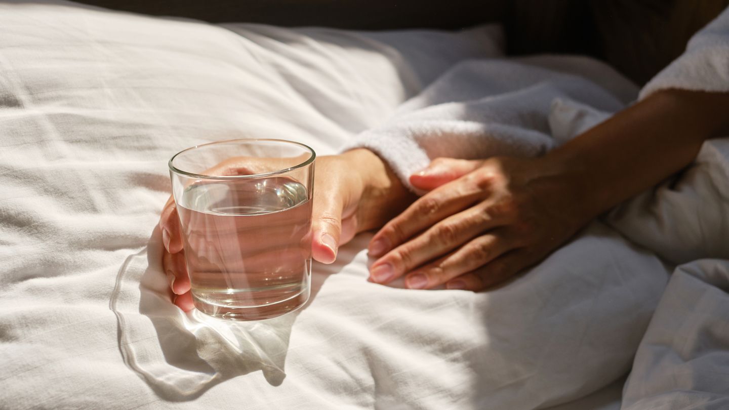 person in bed holding a glass of water